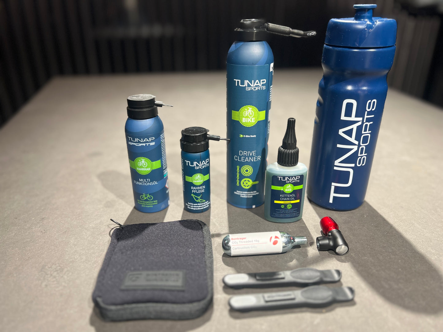 Verscheidene Reinigungs- und Pflegemittel fürs Fahrrad vom Hersteller Tunap. Ebenfalls zu erkennen ist ein Notfall-Reparaturkit für Reifen und eine blaue Trinkflasche mit dem Tunap Sports Schriftzug.