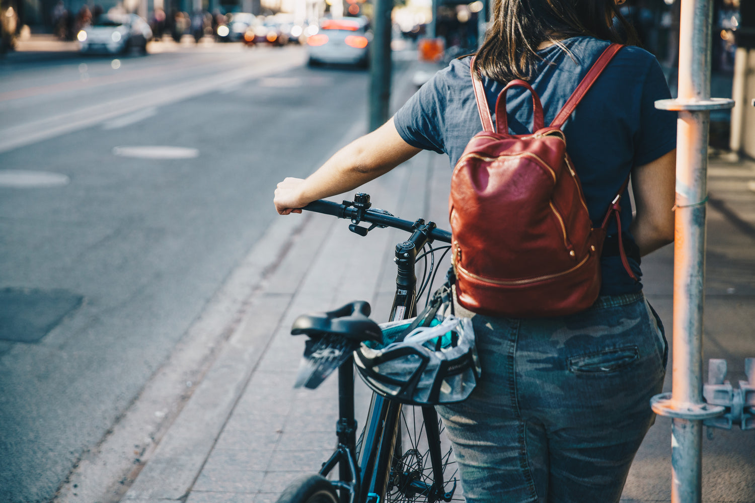 Frau mit kleinem Lederrucksack schiebt ihr Rad auf dem Gehweg
